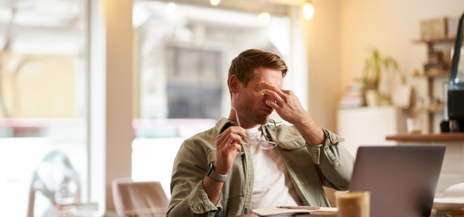 portrait tired man rubbing his eyes after looking laptop screen working computer sitting cafe having break taking off his glasses(1)